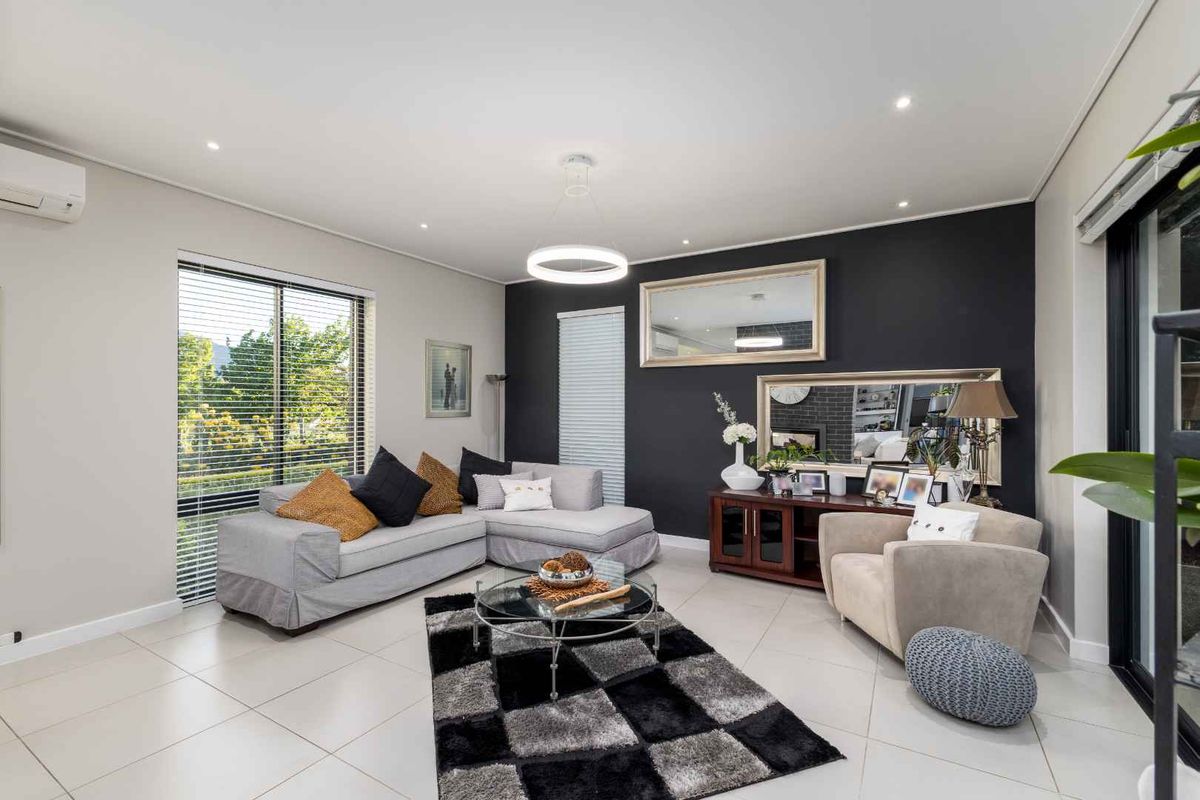 A well-maintained living room featuring tiled flooring, recessed downlighting, a split-system air conditioner, and large sliding glass doors providing natural light.