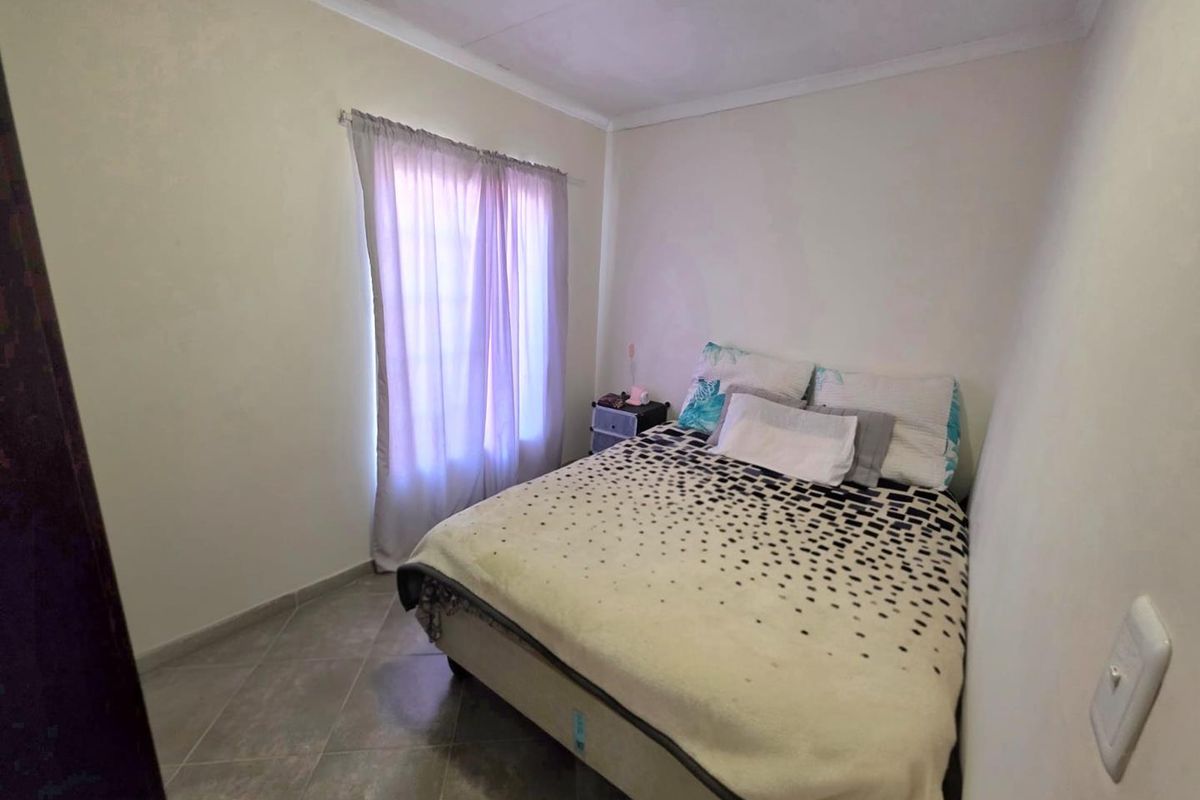 A compact bedroom featuring tiled flooring and neutral wall finishes, providing a functional space with natural light from the window.