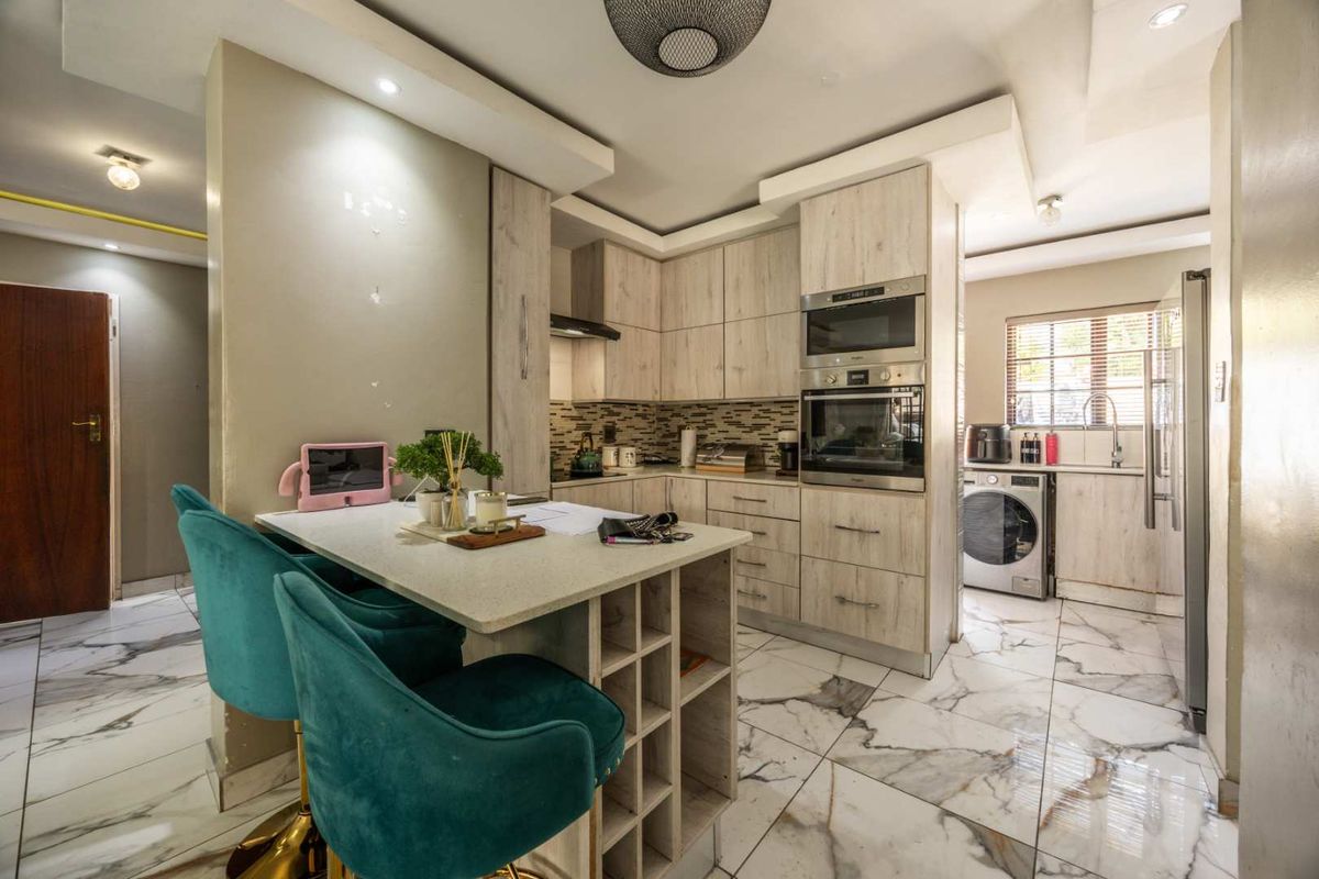 Modern kitchen featuring light wood-grain cabinetry, stone countertops, integrated appliances, and elegant marble-look floor tiles with a functional breakfast bar island.