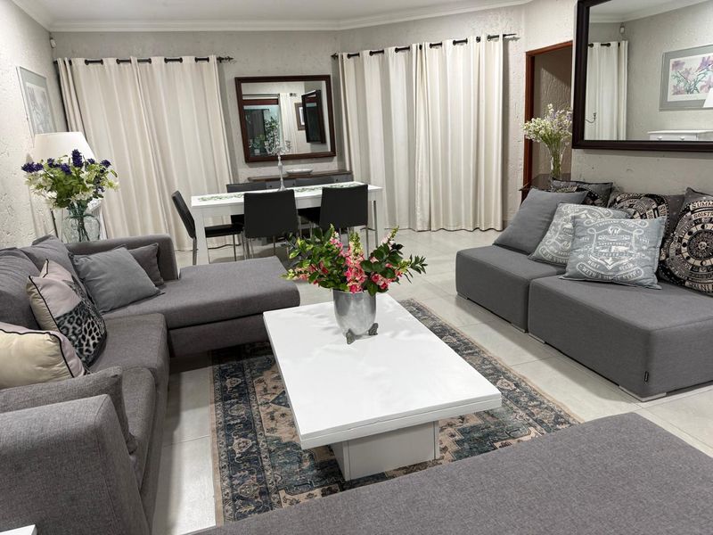 Spacious open-plan living and dining area featuring neutral tiled flooring, decorative cornicing, and large windows dressed with floor-to-ceiling curtains.