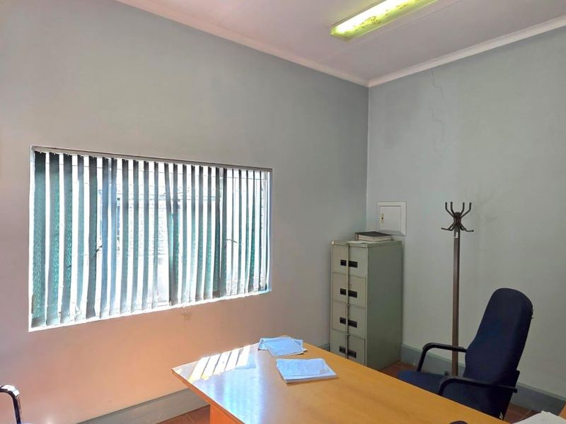 A functional office space featuring a window-mounted air conditioning unit, vertical blinds, and basic overhead lighting, suitable for a professional workspace.