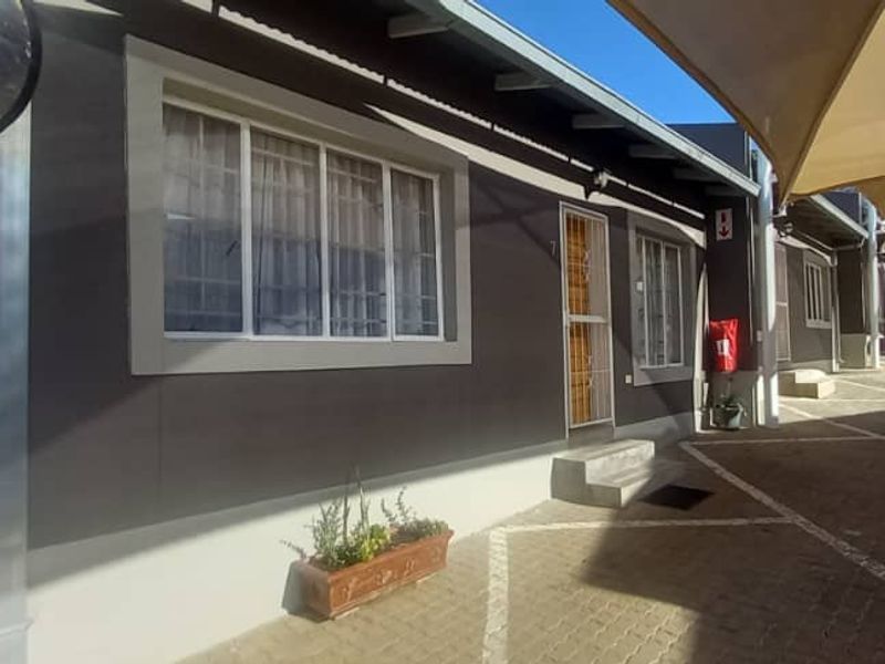 Front exterior view of the townhouse featuring a paved driveway, covered parking with shade sails, and secure entrance access.