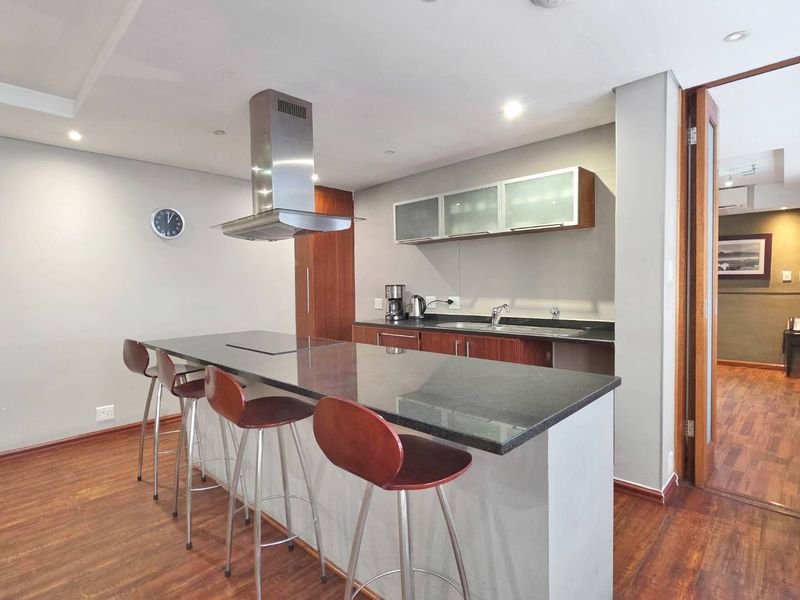 Modern kitchen featuring a central island with granite countertops, stainless steel extractor fan, and ample built-in cabinetry, complemented by warm laminate flooring.