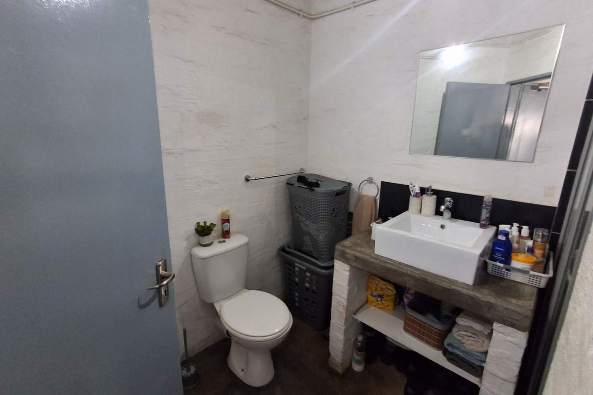 A compact bathroom featuring a concrete vanity with a vessel sink, wall-mounted mirror, and standard toilet, finished with rustic exposed masonry walls.