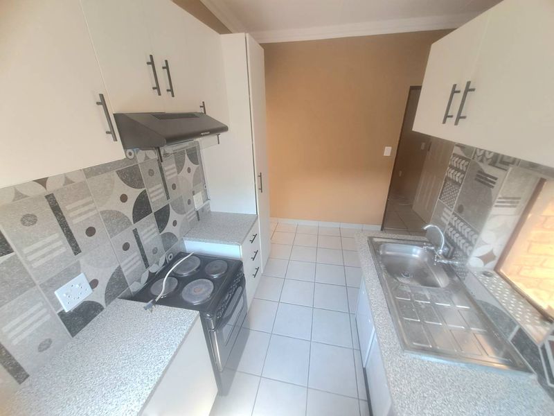 A compact, functional kitchen featuring white cabinetry, patterned tiled backsplash, laminate countertops, and a built-in electric stove with an extractor fan.