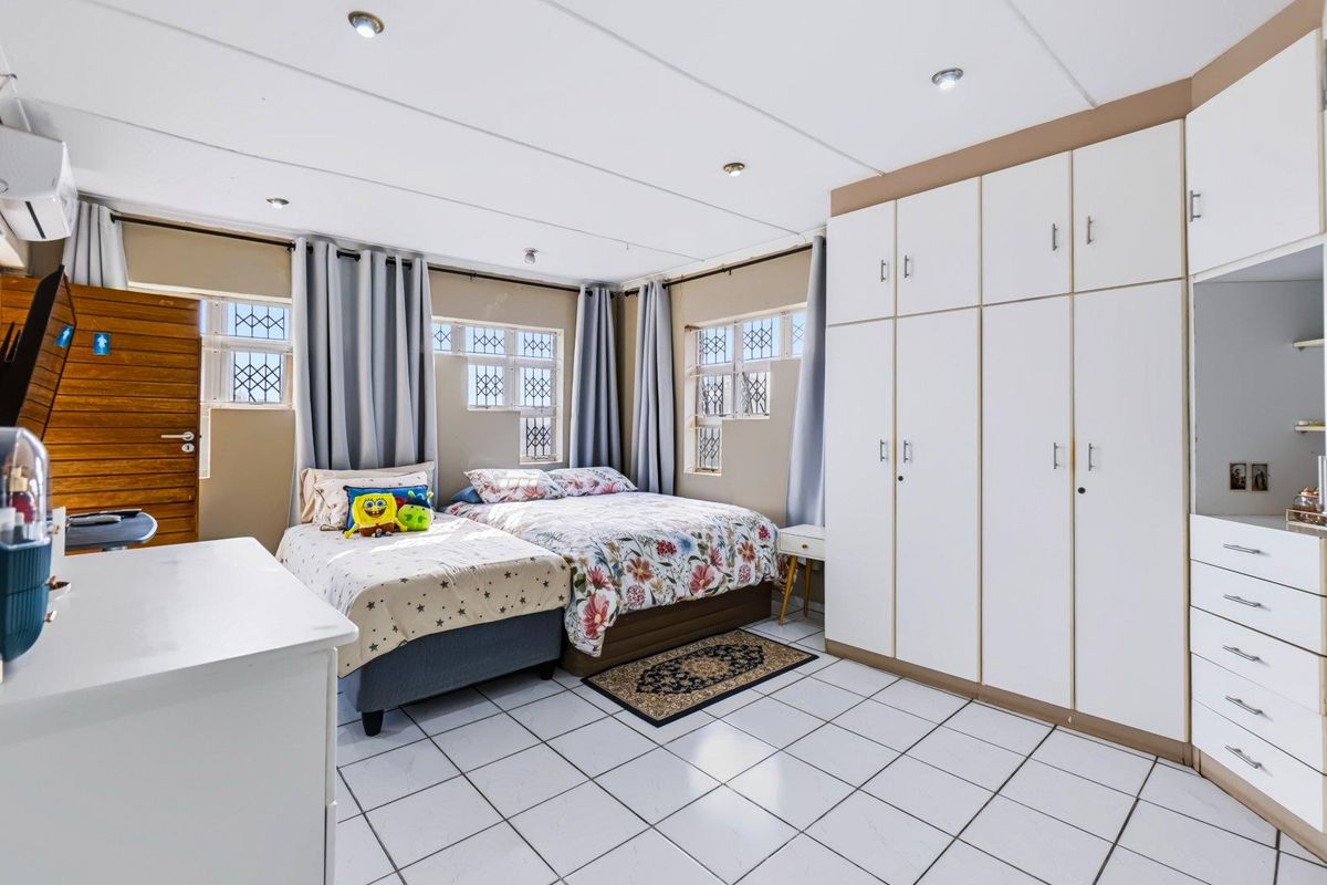Spacious bedroom featuring tiled flooring, extensive built-in cupboards, recessed lighting, and security bars on the windows.