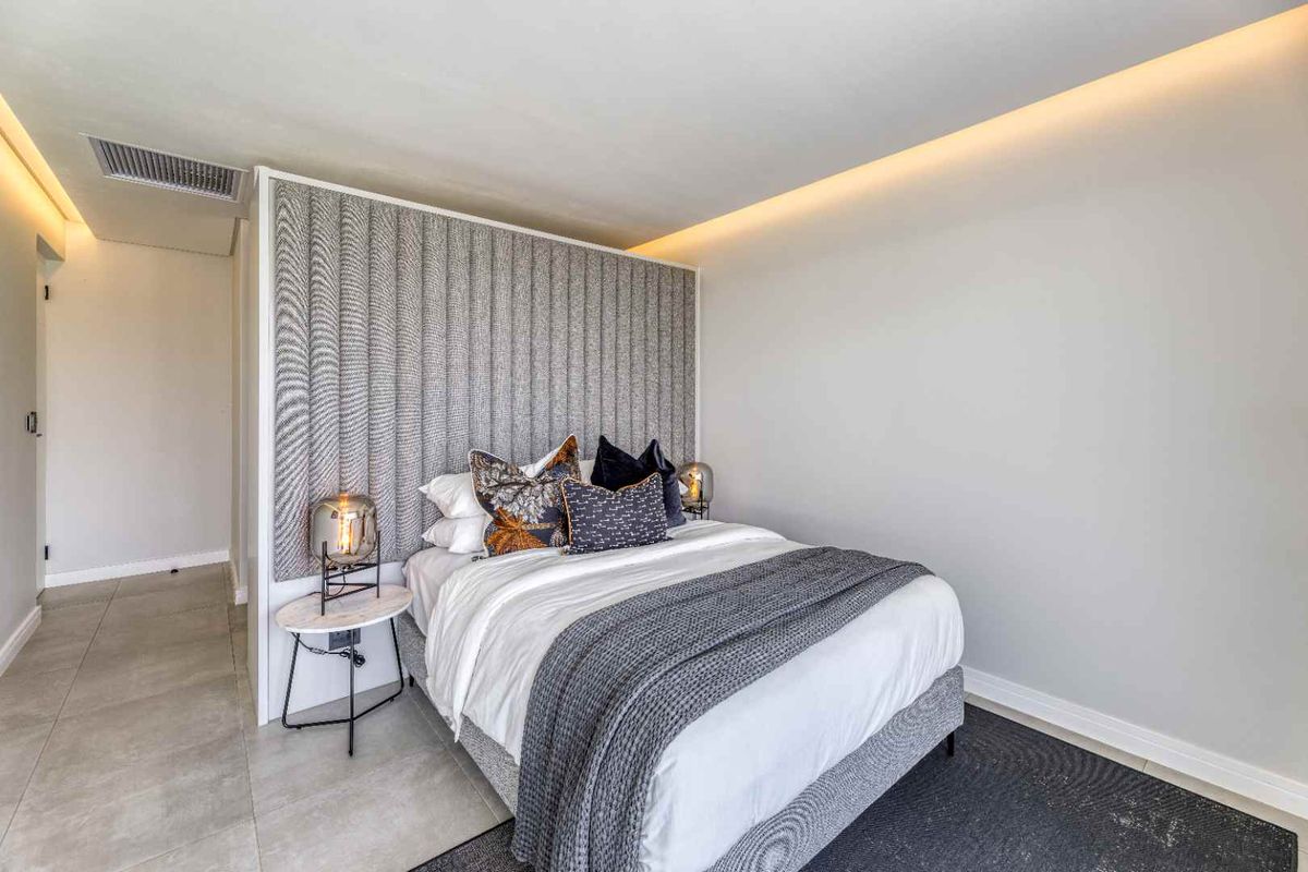 Modern bedroom featuring a textured upholstered feature wall, recessed cove lighting, and neutral floor tiling.