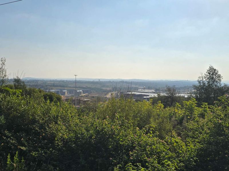 An elevated landscape view overlooking the surrounding area, featuring natural vegetation and distant urban development.