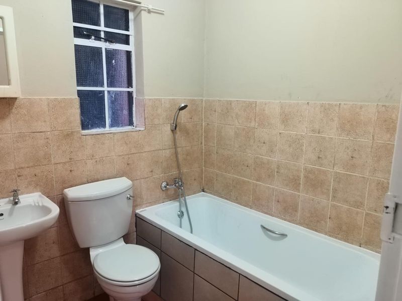 A functional bathroom featuring a pedestal basin, toilet, and bathtub with a handheld shower mixer, finished with neutral wall tiling.