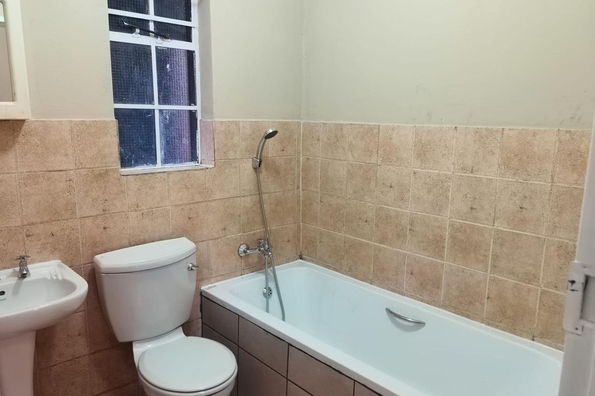 A functional bathroom featuring a pedestal basin, toilet, and bathtub with a handheld shower mixer, finished with neutral wall tiling.