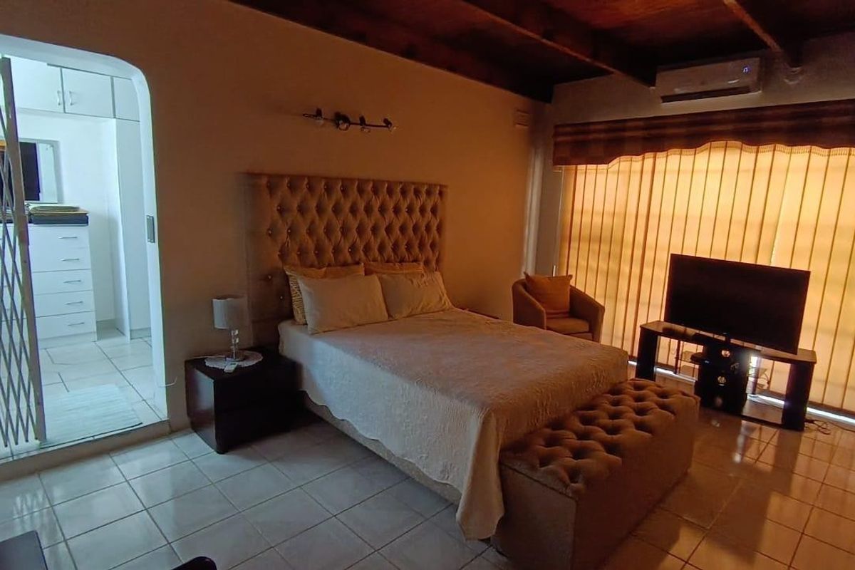 Spacious bedroom featuring exposed timber ceiling beams, tiled flooring, and a split-system air conditioning unit with access to an adjoining area.