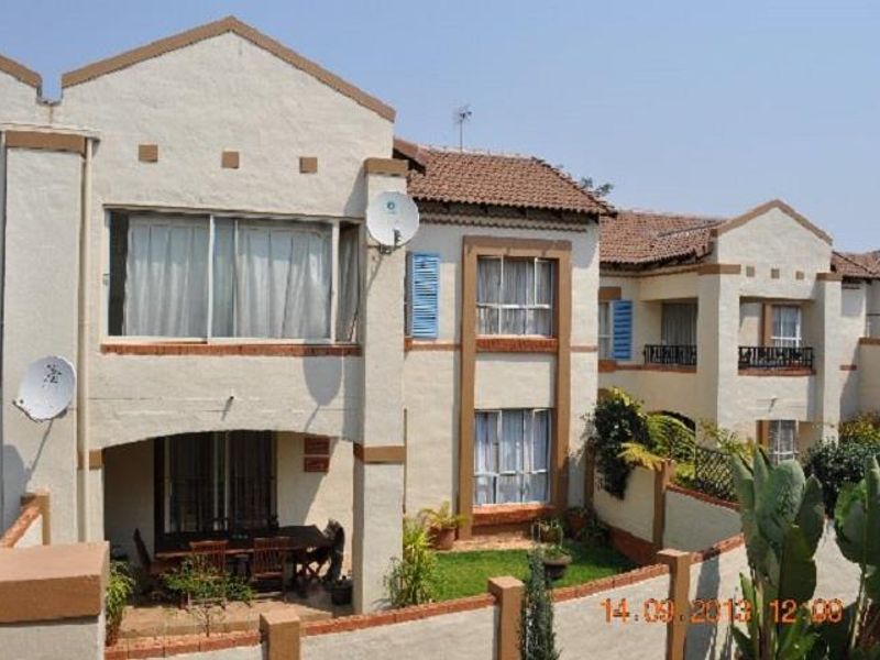 Rear view of a multi-story apartment complex featuring stucco facades, terracotta roof tiles, covered patios, and private garden spaces with boundary walls.