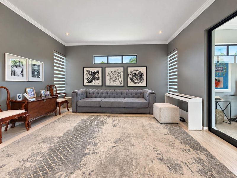 A well-maintained living room featuring neutral grey walls, crown molding, recessed lighting, and large windows with modern blinds.