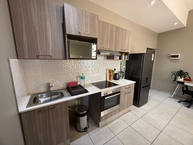 Modern kitchen featuring wood-grain cabinetry, integrated appliances including an oven and hob, tiled backsplash, and neutral floor tiles.