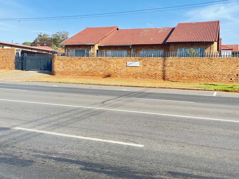 Street view of a face-brick townhouse complex featuring a tiled roof, secure boundary wall with spikes, and gated driveway access.