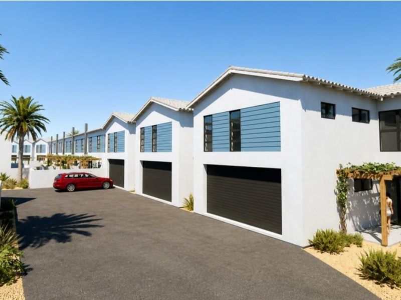A modern townhouse complex featuring clean white facades, dark garage doors, and timber pergola accents, set against a paved driveway.