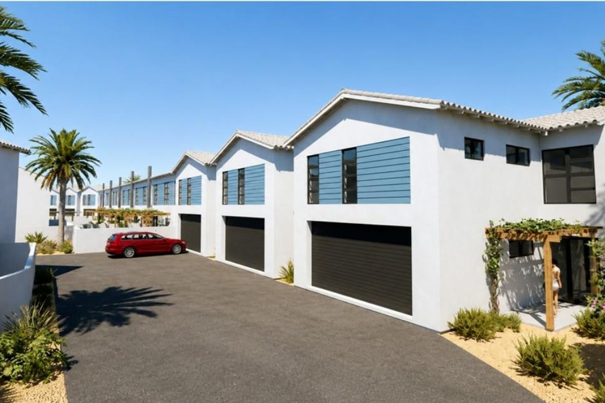 A modern townhouse complex featuring clean white facades, dark garage doors, and timber pergola accents, set against a paved driveway.