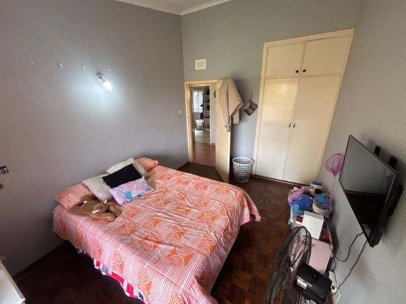 A bedroom featuring parquet flooring, a built-in wardrobe, and a wall-mounted light fixture, offering a functional space with potential for cosmetic updates.