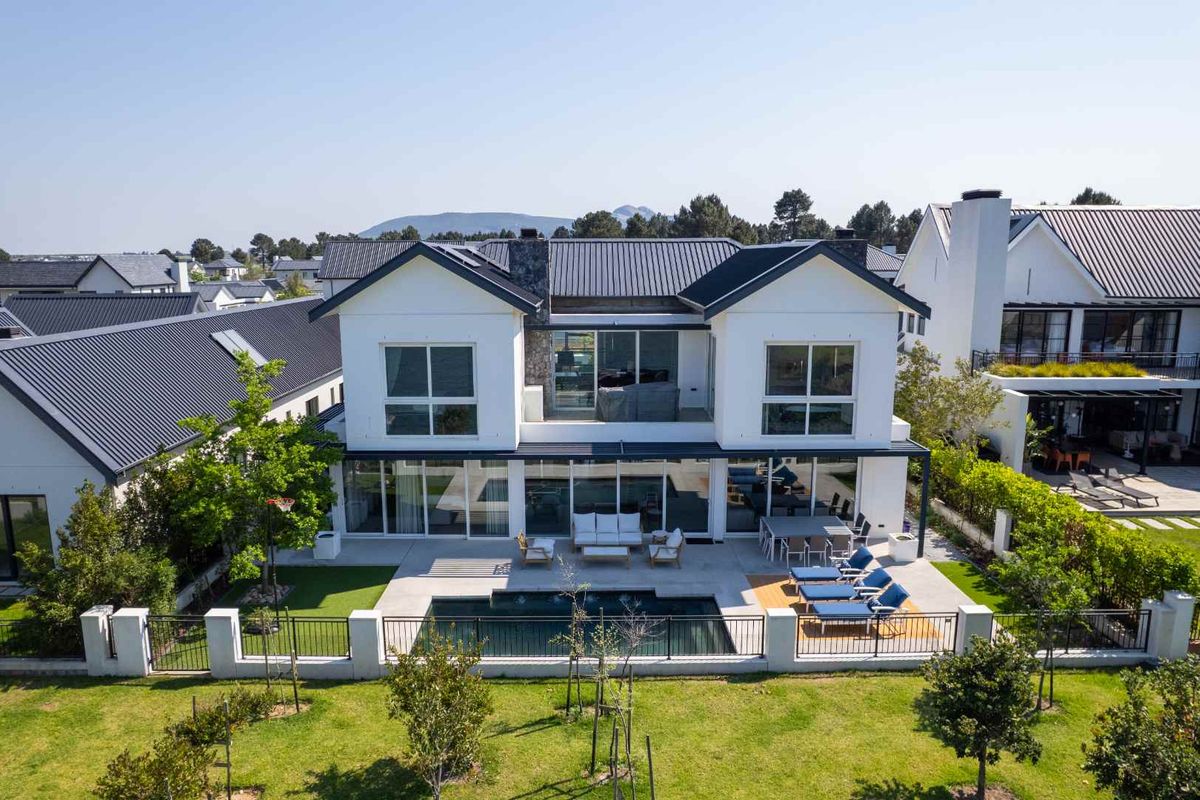 Aerial view of the rear elevation featuring a modern two-story home with a swimming pool, paved patio area, and landscaped garden.