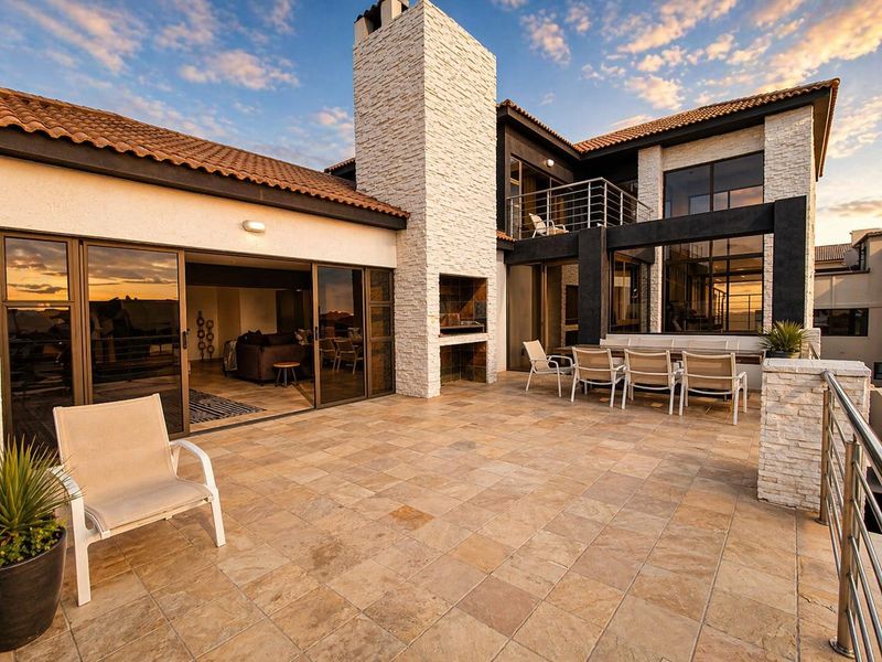 Spacious outdoor patio featuring a stone-clad fireplace, built-in braai, and seamless access to the interior living area through large sliding glass doors.