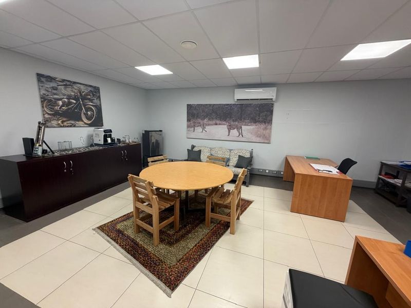 A functional office space featuring tiled flooring, a suspended ceiling with recessed lighting, and a wall-mounted air conditioning unit.