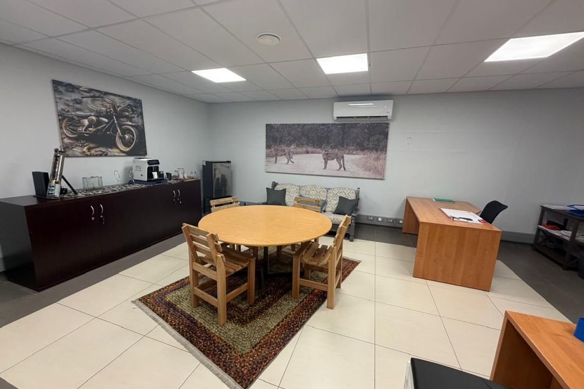 A functional office space featuring tiled flooring, a suspended ceiling with recessed lighting, and a wall-mounted air conditioning unit.
