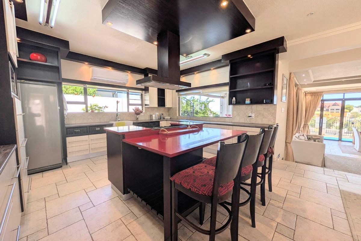 Modern kitchen featuring a central island with a red countertop, dark cabinetry, stone tile flooring, and integrated lighting, flowing into an adjacent living area.
