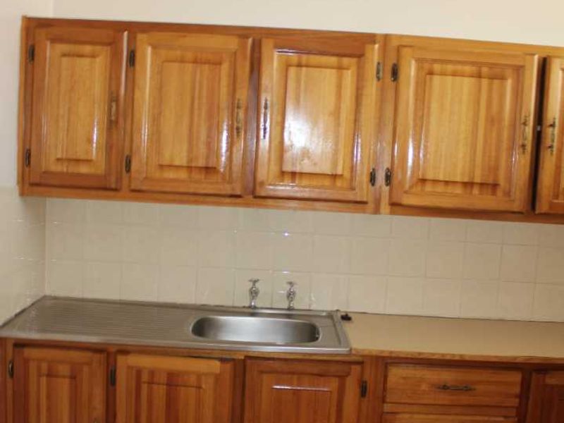 A functional kitchen area featuring traditional wooden cabinetry, a stainless steel sink, and a tiled backsplash, offering a blank canvas for modern updates.