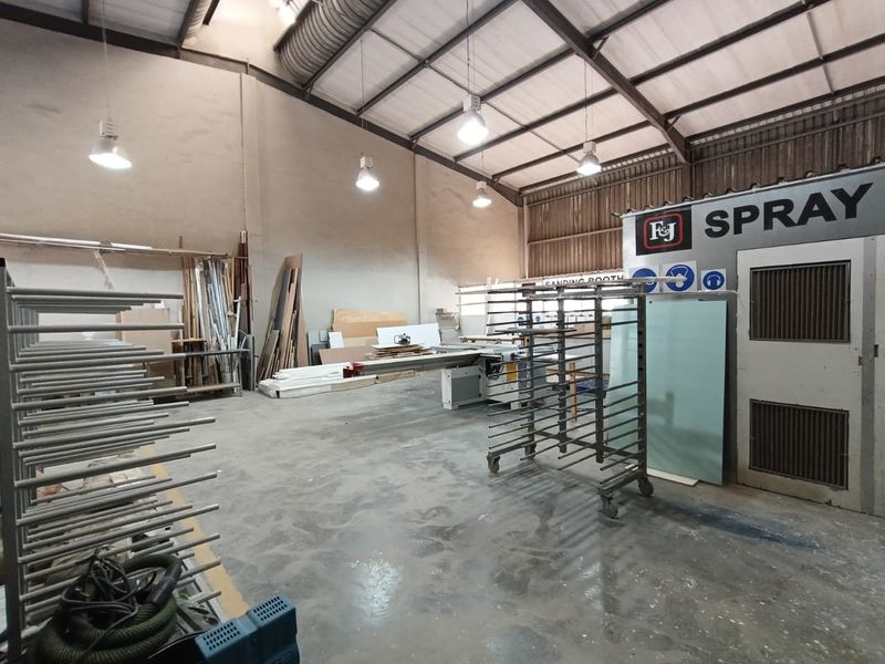 Industrial workshop space featuring a dedicated spray booth, high-bay lighting, exposed steel roof structure, and durable concrete flooring suitable for manufacturing or fabrication.