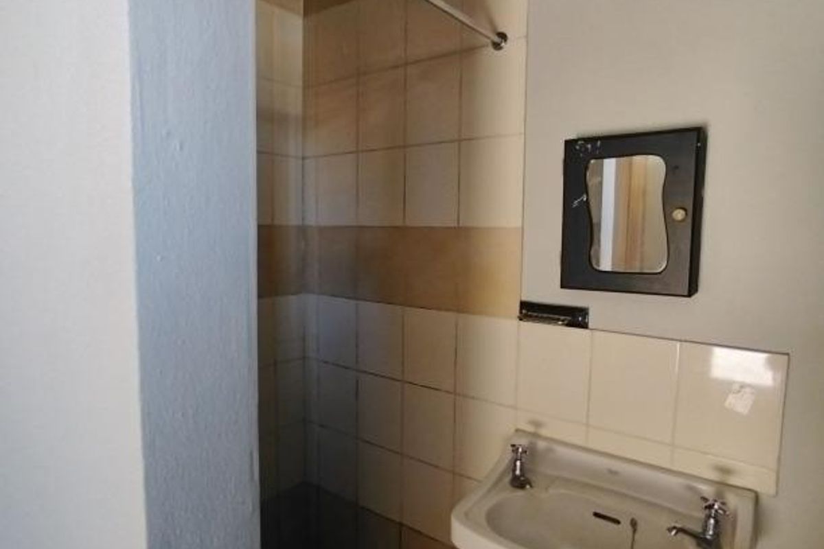A functional bathroom featuring a pedestal basin and a tiled shower area, presenting an opportunity for modernization and cosmetic updates.