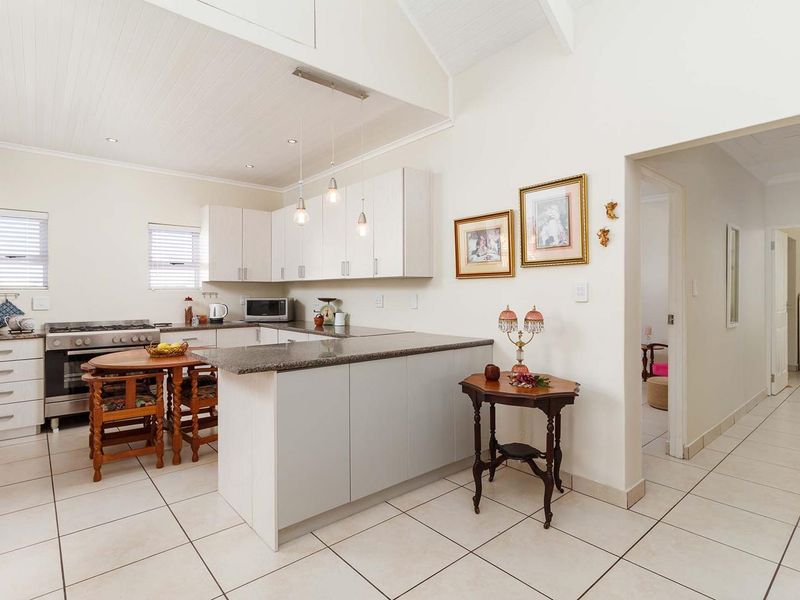 A bright, open-plan kitchen featuring granite countertops, white cabinetry, a gas stove, and vaulted ceilings with recessed and pendant lighting.