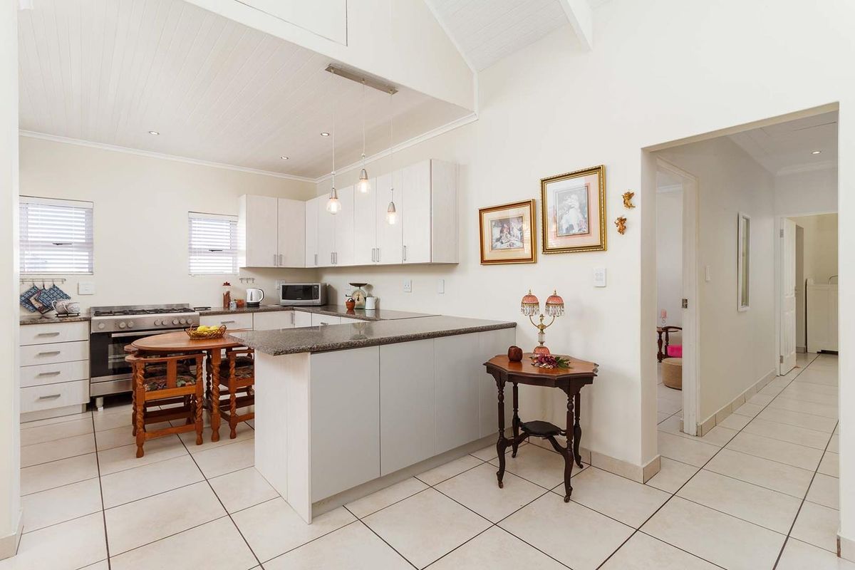 A bright, open-plan kitchen featuring granite countertops, white cabinetry, a gas stove, and vaulted ceilings with recessed and pendant lighting.