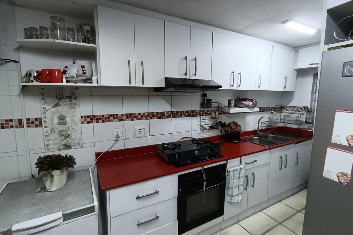 A functional kitchen featuring white cabinetry, a contrasting red countertop, built-in oven, gas hob, and tiled backsplash with integrated sink.