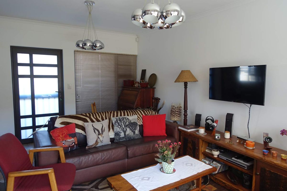 A comfortable living room featuring a glass-paneled exterior door, horizontal window blinds, and modern pendant lighting fixtures.