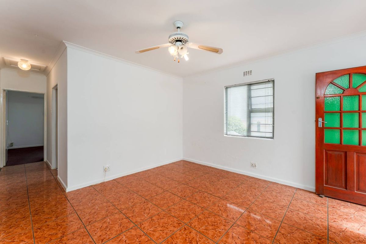 A bright, empty bedroom featuring tiled flooring, a ceiling fan, and a classic wooden door with glass inserts.