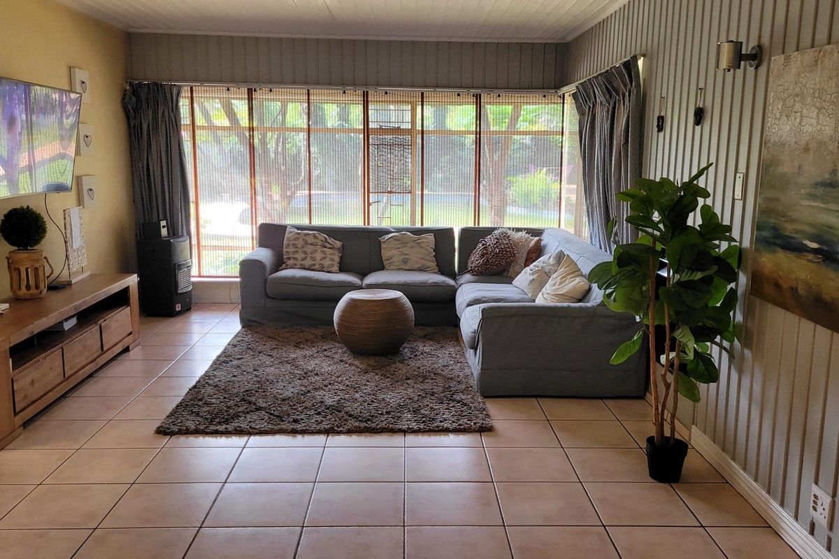 A comfortable living room featuring large windows with natural light, tiled flooring, and vertical wall paneling, creating a relaxed and functional living space.
