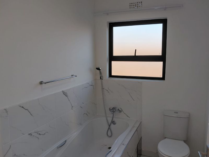 A clean, modern bathroom featuring a bathtub with handheld shower attachment, marble-look wall tiling, and a standard toilet.