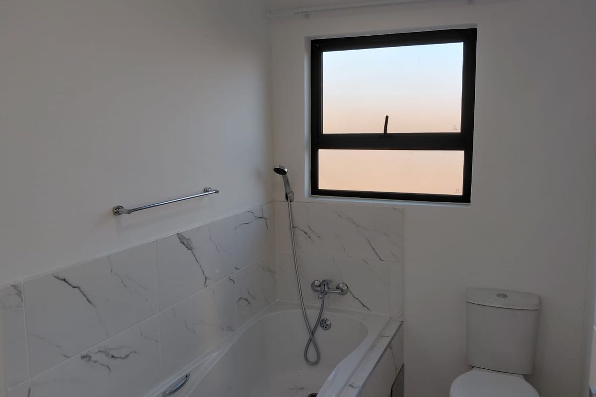A clean, modern bathroom featuring a bathtub with handheld shower attachment, marble-look wall tiling, and a standard toilet.