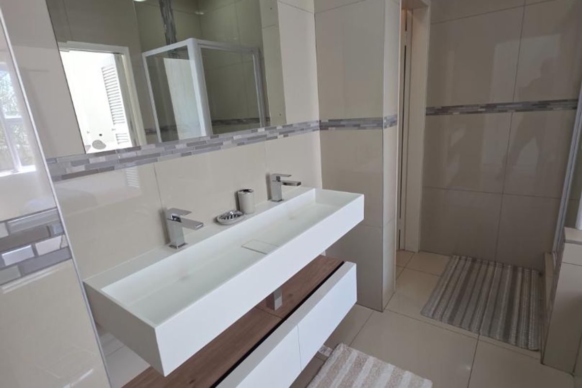 Modern bathroom featuring a sleek double vanity with wall-mounted basins, high-gloss tiled walls, and a separate shower enclosure with contemporary finishes.