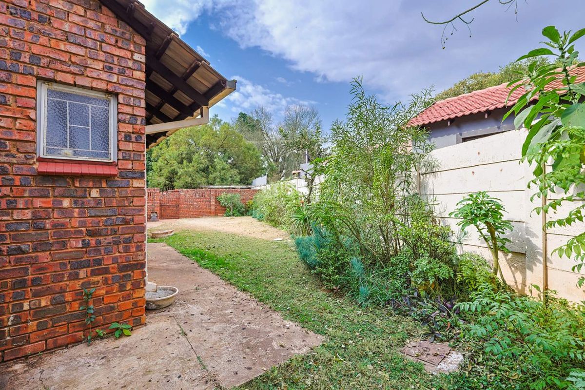 A rear garden area featuring a face brick exterior wall, concrete pathway, and precast boundary wall, requiring landscaping and maintenance.