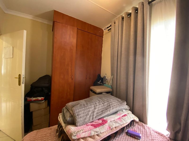 A bedroom featuring a built-in wooden wardrobe and window with curtain rail, providing functional storage and natural light.