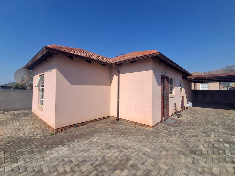 Rear view of the house featuring a paved yard, security gate, and attached carport structure.