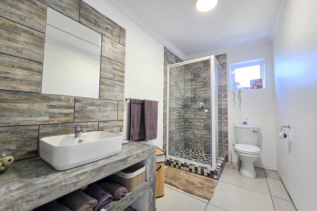 Modern bathroom featuring a concrete-style vanity with vessel sink, walk-in shower with tiled surround, and contemporary fixtures.