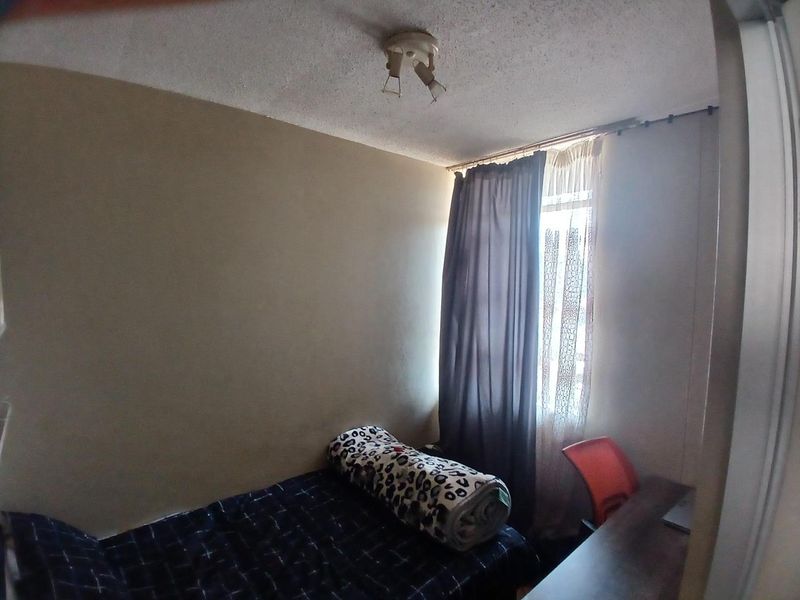 A compact bedroom featuring a textured ceiling, window with curtain rod, and neutral wall finishes, suitable for a single bed or office setup.