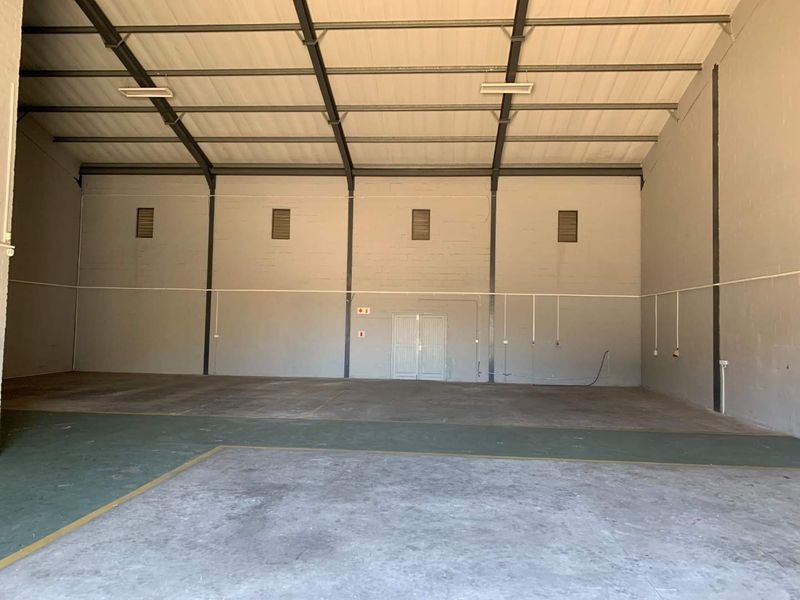 Spacious industrial warehouse unit featuring high ceilings, exposed steel portal frame, concrete flooring, and double door access, suitable for various commercial or storage uses.
