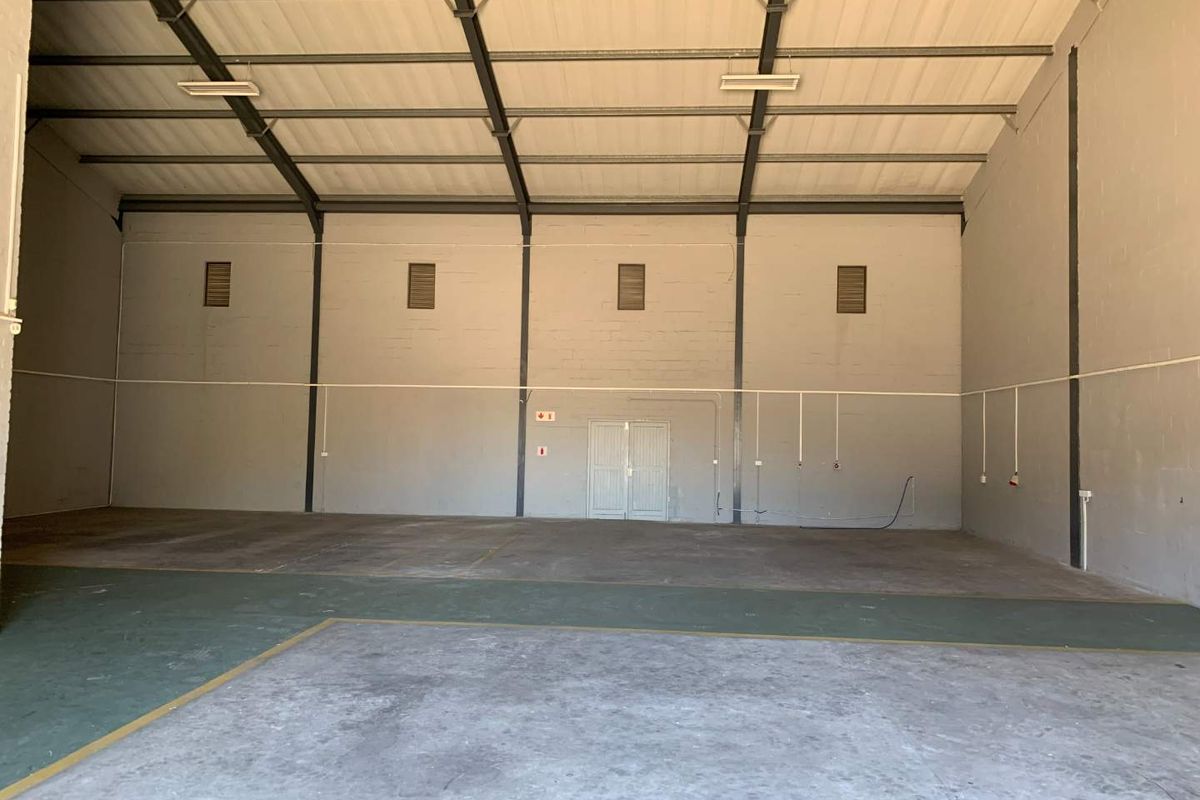 Spacious industrial warehouse unit featuring high ceilings, exposed steel portal frame, concrete flooring, and double door access, suitable for various commercial or storage uses.