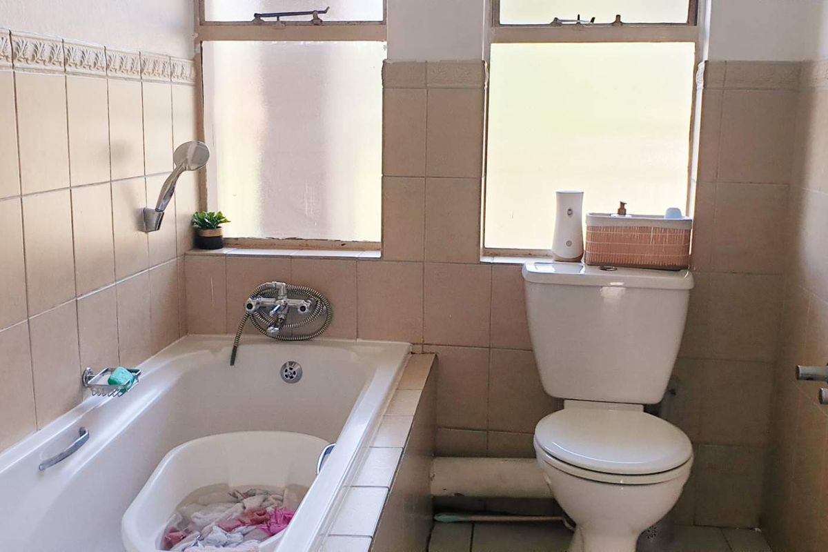 A dated bathroom featuring a built-in bathtub with shower attachment and a standard toilet, finished with neutral wall tiling.