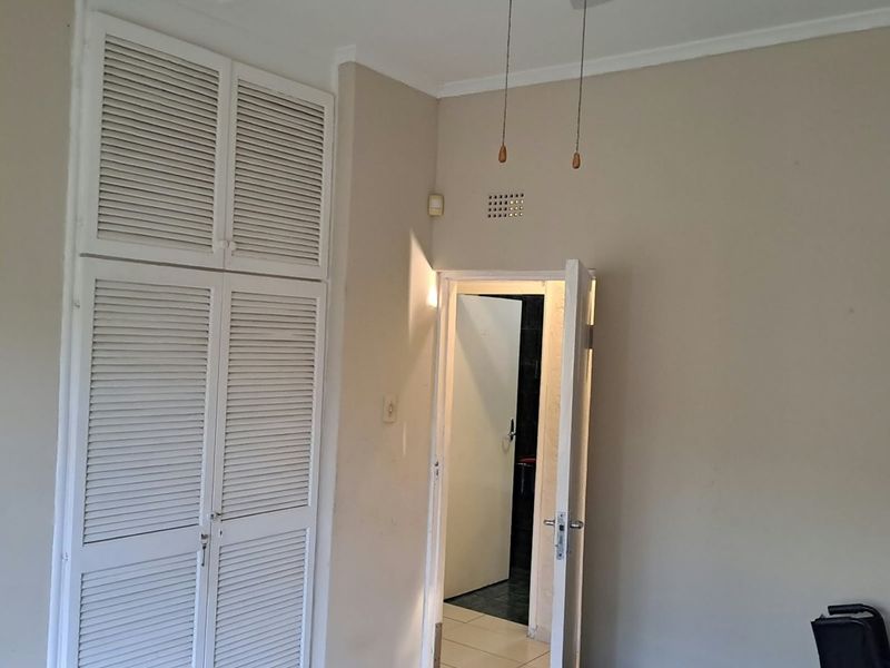 A simple bedroom featuring built-in louvered cupboards, a ceiling fan, and tiled flooring, offering a functional space ready for personalization.