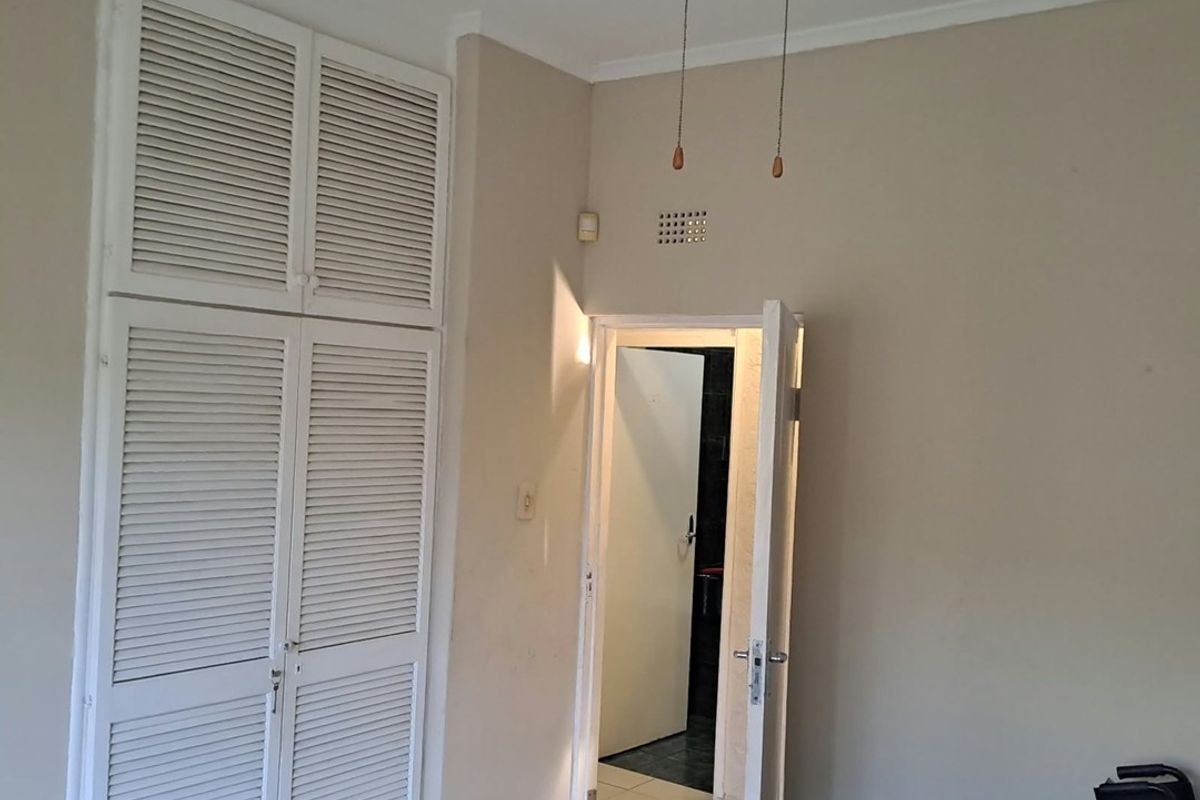 A simple bedroom featuring built-in louvered cupboards, a ceiling fan, and tiled flooring, offering a functional space ready for personalization.