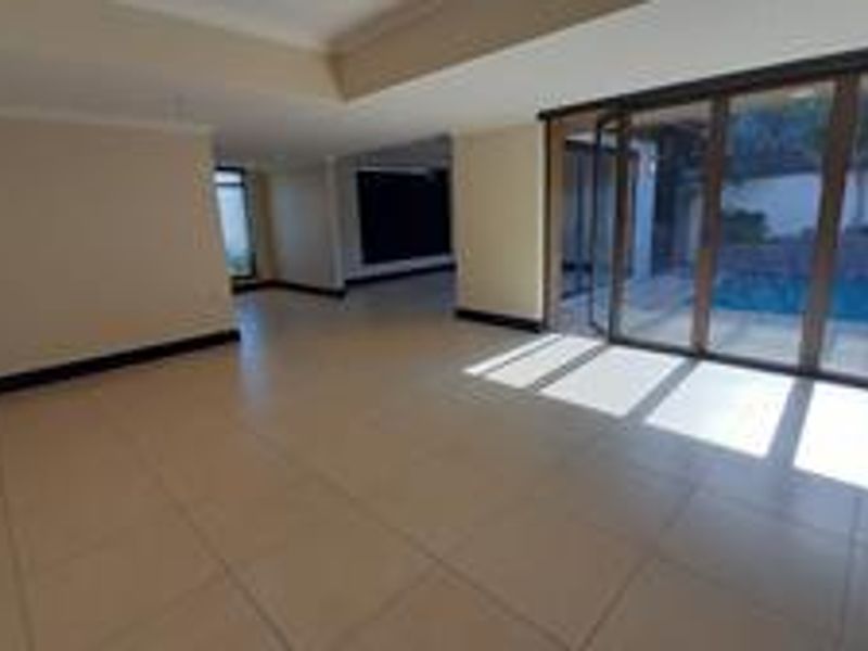 Spacious open-plan living area featuring large format floor tiles, recessed ceiling details, and expansive sliding glass doors providing direct access to the pool area.